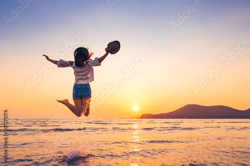 travel women hold hat and jump on the sea wave.