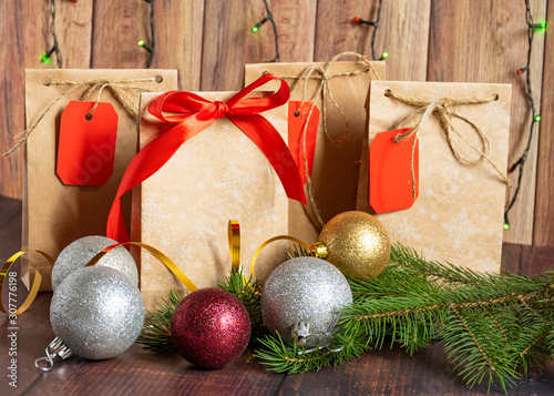 Gift bag made of handmade kraft paper on a wooden background in a Christmas style, decorated with tree balls, cones, a ball of rope, fir branches. Christmas, New Year, winter holiday. Kraft package