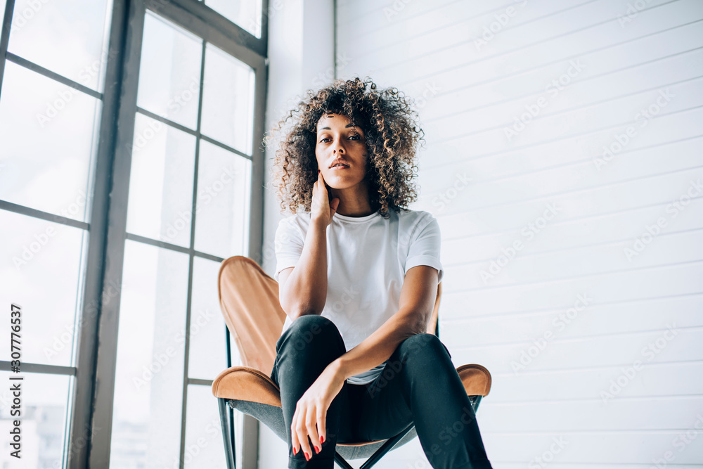 Serious woman sitting and touching neck in studio space Serious woman sitting and touching neck in studio space