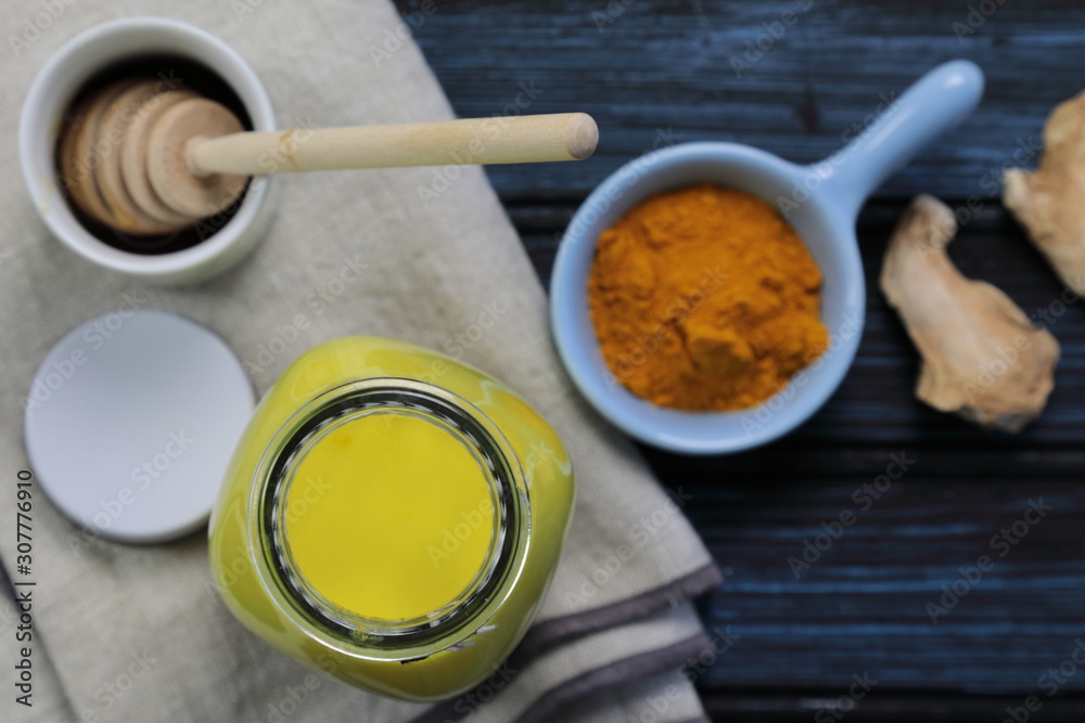 Fototapeta premium Turmeric latte, golden milk or the anti-inflammatory Indian Haldi Doodh with superfood Turmeric powder, Ginder and Cinnamon sweetened with honey on wooden background