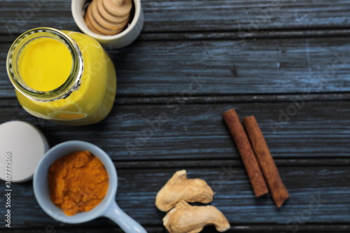 Turmeric latte, golden milk or the anti-inflammatory Indian Haldi Doodh with superfood Turmeric powder, Ginder and Cinnamon sweetened with honey on wooden background