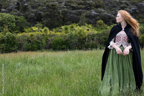 Fotografiet Red-haired 18th century woman in embroidered bodice and standing in long grass i