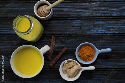 Turmeric latte, golden milk or the anti-inflammatory Indian Haldi Doodh with superfood Turmeric powder, Ginder and Cinnamon sweetened with honey on wooden background