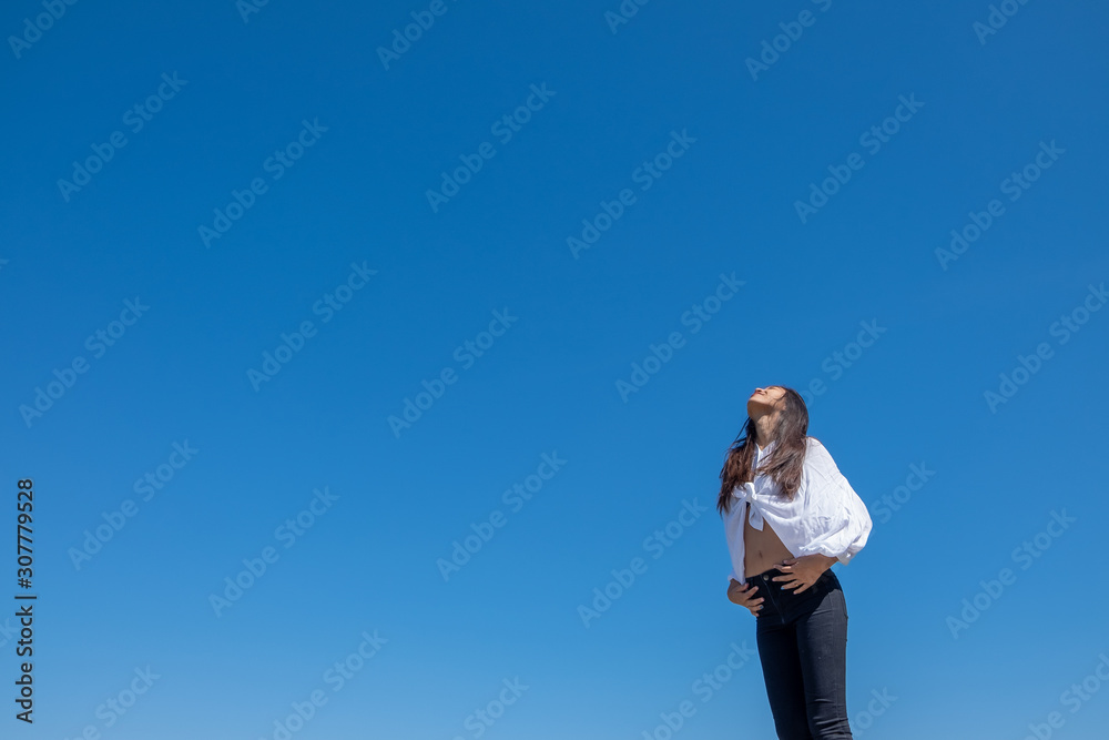 Happy woman with tanned slim body breathing fresh air raising her arms up, enjoying a sunny summer holiday on beach destination against blue sky, outdoors. Travel and well being lifestyle. Happy woman with tanned slim body breathing fresh air raising her arms up, enjoying a sunny summer holiday on beach destination against blue sky, outdoors. Travel and well being lifestyle.