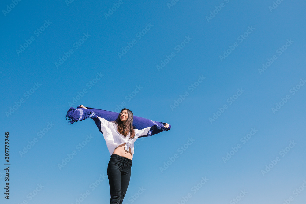 Happy woman with tanned slim body breathing fresh air raising her arms up, enjoying a sunny summer holiday on beach destination against blue sky, outdoors. Travel and well being lifestyle. Happy woman with tanned slim body breathing fresh air raising her arms up, enjoying a sunny summer holiday on beach destination against blue sky, outdoors. Travel and well being lifestyle.