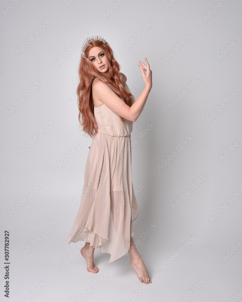 full length portrait of a pretty, fairy girl wearing a nude flowy dress and crystal crown. Standing and dancing pose against a grey studio background. full length portrait of a pretty, fairy girl wearing a nude flowy dress and crystal crown. Standing and dancing pose against a grey studio background.