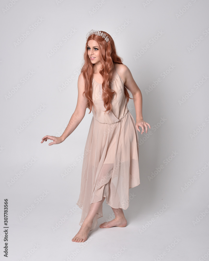 full length portrait of a pretty, fairy girl wearing a nude flowy dress and crystal crown. Standing and dancing pose against a grey studio background. full length portrait of a pretty, fairy girl wearing a nude flowy dress and crystal crown. Standing and dancing pose against a grey studio background.