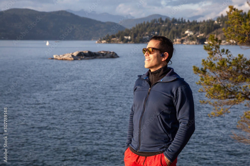 Portrait of an Adventurous Latin Man outside in nature during a cloudy and sunny sunset. Taken in Lighthouse Park, Horseshoe Bay, West Vancouver, BC, Canada. Portrait of an Adventurous Latin Man outside in nature during a cloudy and sunny sunset. Taken in Lighthouse Park, Horseshoe Bay, West Vancouver, BC, Canada.