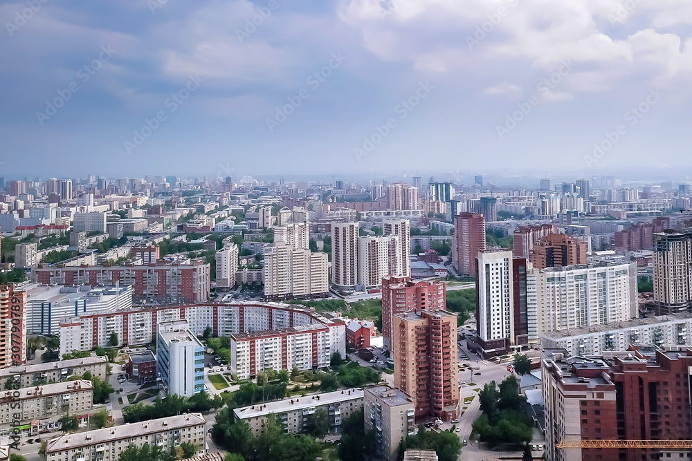 Aerial view of the landscape in a big city with high houses and skyscrapers in the center of Novosibirsk under a cloudy sky with fog and haze on a summer cloudy day.