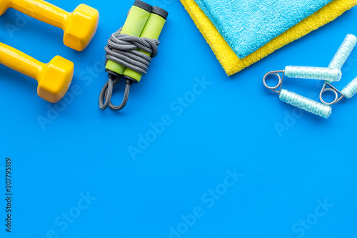 Gym equipment - dumbbells, jump rope - frame on blue background top-down copy space