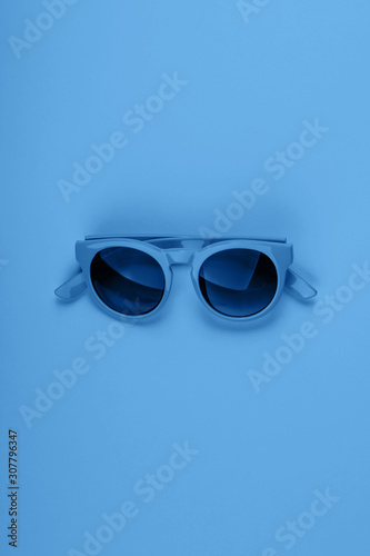 Classic blue color of 2020 sun glasses. Monochrome minimal fashion flat lay.