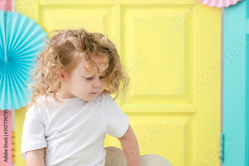 Pretty little blonde curly girl portrait in white t-shirt on yellow background.