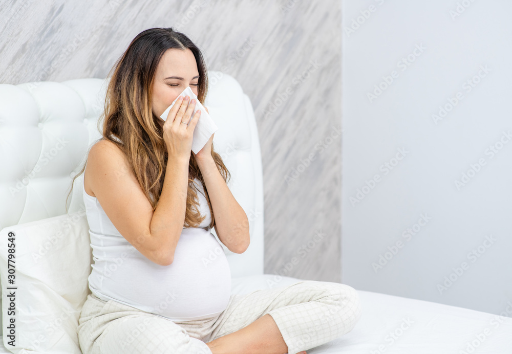 pregnant woman blows her nose while sitting on the bed pregnant woman blows her nose while sitting on the bed
