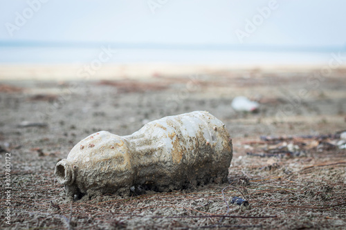 Plastic bottles sink in a pile of sand on the beach.