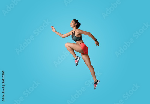 Fototapeta Naklejka Na Ścianę i Meble -  Athletic young woman running on light blue background, side view