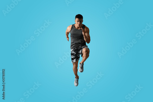 Athletic young man running on light blue background