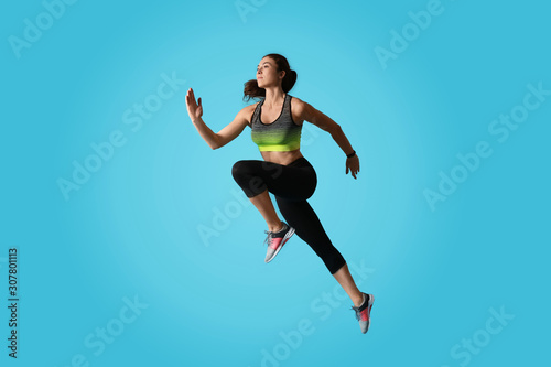 Athletic young woman running on light blue background  side view