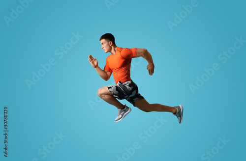 Athletic young man running on light blue background, side view