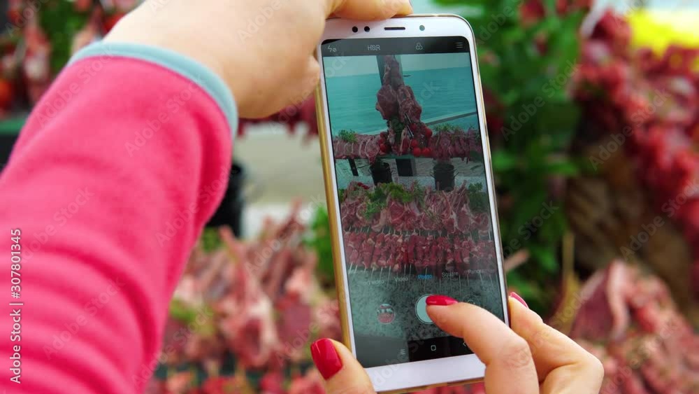 A woman photographs on the smartphone rows of delicious raw lamb for a barbecue or grill. Social network blogger concept photo. A woman photographs on the smartphone rows of delicious raw lamb for a barbecue or grill. Social network blogger concept photo.