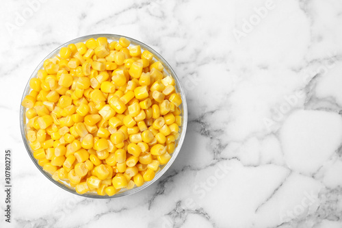 Delicious canned corn in bowl on marble table, top view. Space for text