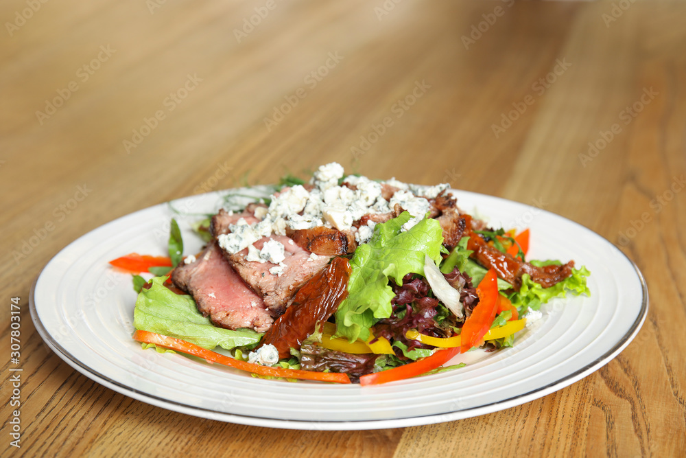 Delicious salad with roasted meat and vegetables served on wooden table