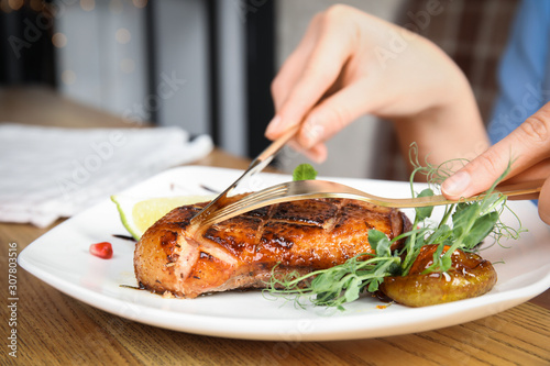 Woman eating delicious grilled duck breast served at wooden table, closeup