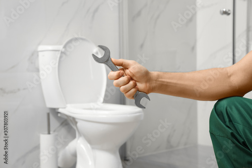 Professional plumber holding wrench near toilet bowl in bathroom  closeup