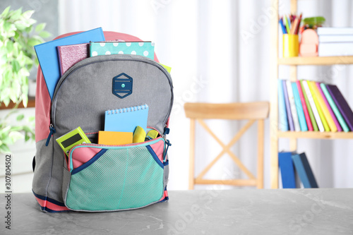 Stylish backpack with different school stationery on table indoors. Space for text