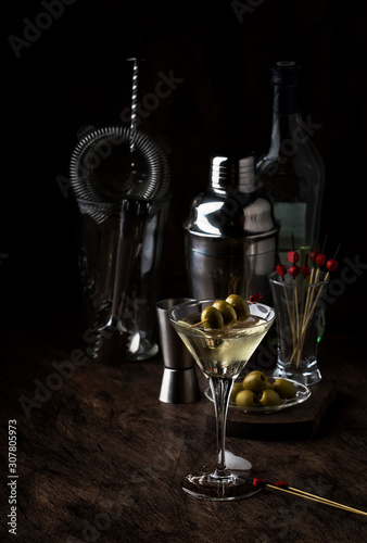 Classic Martini vodka cocktail, with dry vermouth, vodka and green olives, bar tools, vintage wood bar counter, selective focus