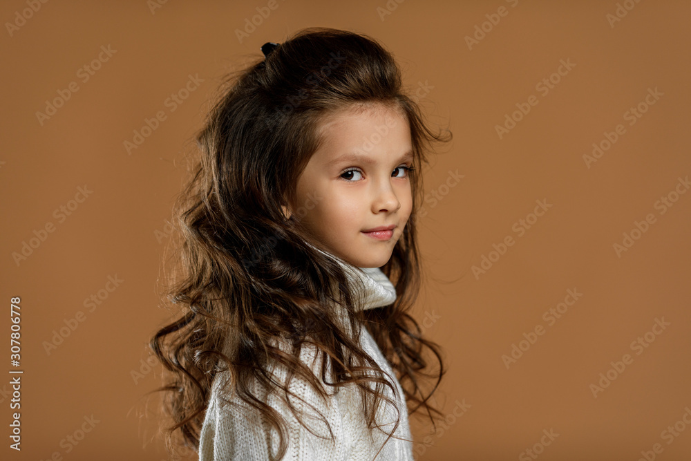 profile of cute smiling little child girl in white sweater looking to camera on beige background. Human emotions and facial expression