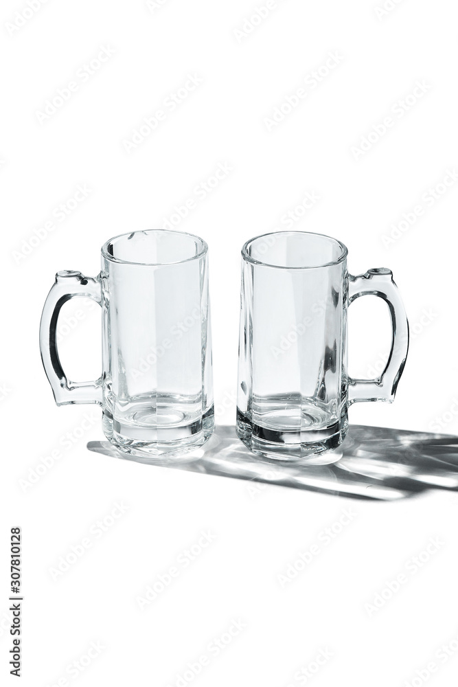 Detailing shot of a pair of classic design beer mugs with thick glass handles. The beer glasses are isolated on the white surface with shadows. Detailing shot of a pair of classic design beer mugs with thick glass handles. The beer glasses are isolated on the white surface with shadows.