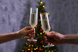 Cropped chot of couple in love clinking champage glasses, toasting next to Christmas tree, wearing themed sweaters. Man and woman celebrating new year. Close up, copy space, grunged wall background.