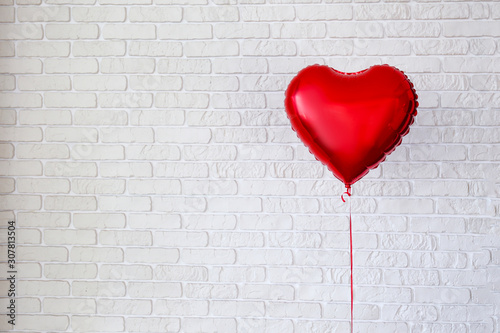 Celebrating Saint Valentine's Day with heart shaped red foil air balloon. Gift for loved woman on special occasion with romantic symbols, Women`s day. Close up, copy space, background, isolated.