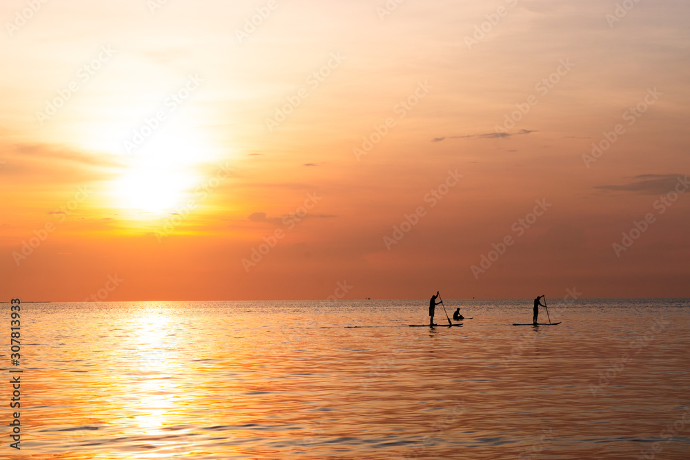 Silhouette of family playing the stand-up paddle board on the sea with beautiful summer sunset colors. Happy family concept.