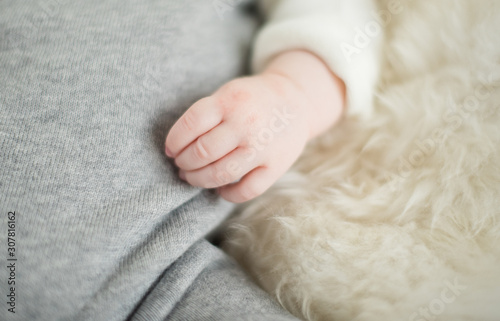 A beautiful soft delicate warm young baby hand photographed with a shallow depth of field. gentle calm colours and feel. baby care and well being. babies hands on a cream fur rug.