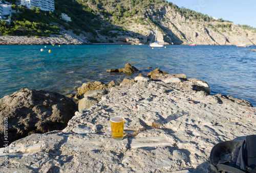 A relaxing Mediterranean sea view, drinking beer on the rocks on a sunny summers evening. Blue waters and rocky mountain views. Drinking alcohol on holiday whilst abroad on vacation.
