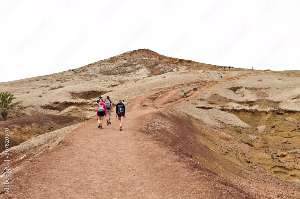 A group of hikers are walking along a desert pathway with volcanic rocks and sand dunes in Madeira Island (Ponta de Sao Lourenco, Portugal, Europe)