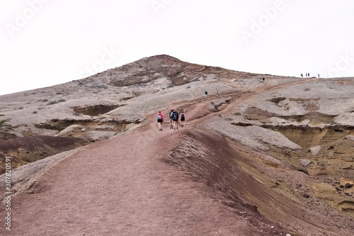 A group of hikers are walking along a desert pathway with volcanic rocks and sand dunes in Madeira Island (Ponta de Sao Lourenco, Portugal, Europe)