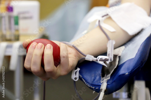 Blood donor during donation with a red bouncy ball in hand. Concept of donorship, transfusion, health care