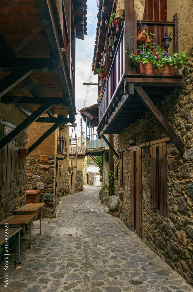 Fototapeta premium Ancient village Kakopetria in Cyprus - travel architecture background. Stunning view of the street in old town. Pots with flowers standing on paved pavement along stone wall