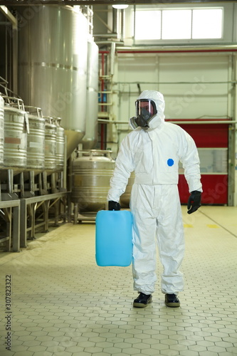 worker in chemical protection suit and mask holds reagent canister in a factory © Петр Смагин