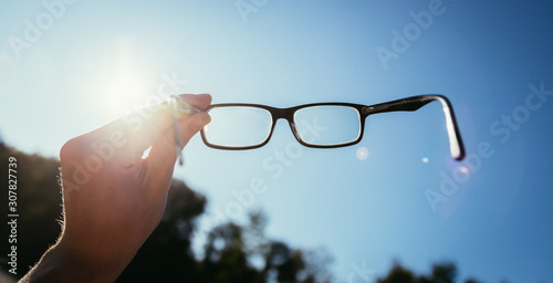 Hand holding glasses outdoors, blue sky, sunbeam with lens flares