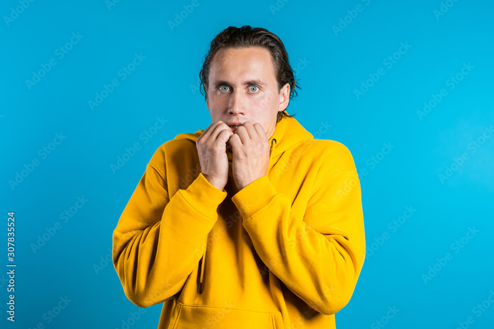 Frightened european man afraid of something and looks into camera with big eyes full of horror over blue wall background.