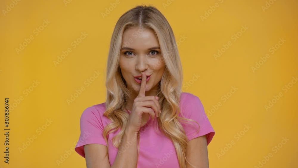 smiling woman showing shh gesture isolated in yellow smiling woman showing shh gesture isolated in yellow