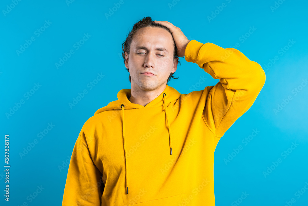 Young guy holding hands on his head because of headache, pain. He is ill. Depressed lost man in yellow hoodie. Drama, emotions concept. 