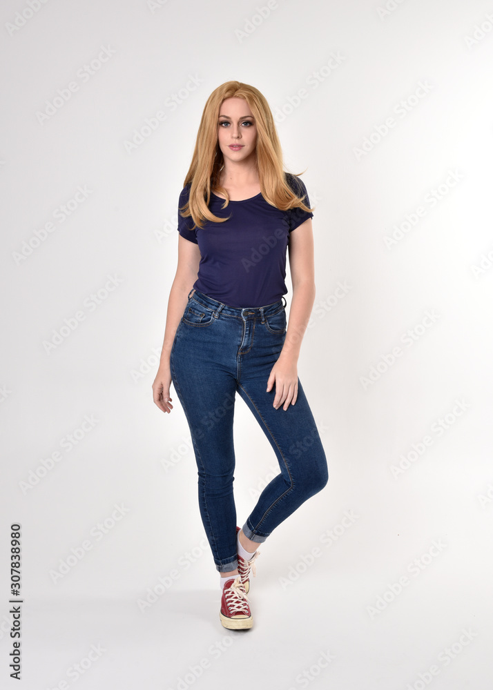 Full length portrait of a pretty blonde girl wearing casual blue shirt, denim jeans and sneakers. Standing pose on a studio background. Full length portrait of a pretty blonde girl wearing casual blue shirt, denim jeans and sneakers. Standing pose on a studio background.