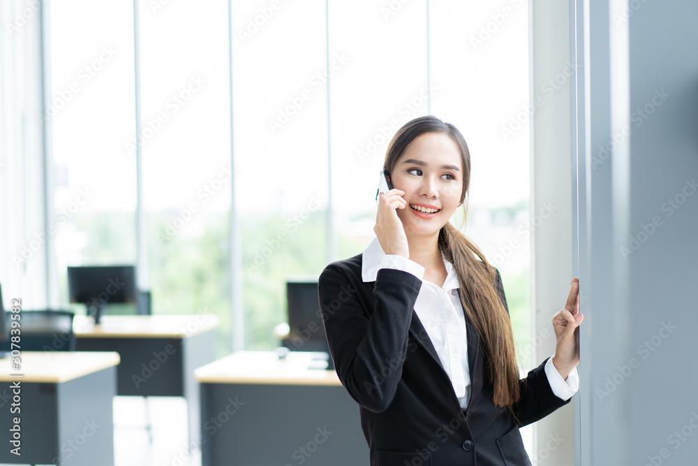 Beautiful Asian businesswoman talking on smartphone near window in the office. Modern businesspeople conconept. Beautiful Asian businesswoman talking on smartphone near window in the office. Modern businesspeople conconept.