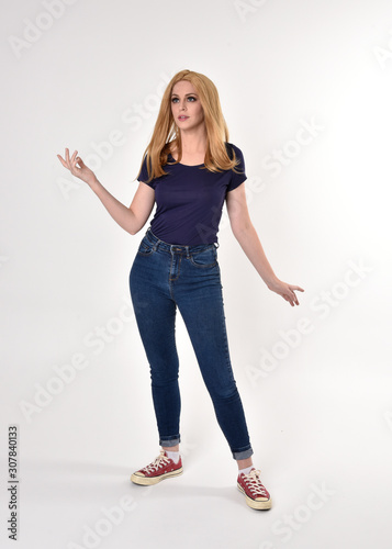 Full length portrait of a pretty blonde girl wearing casual blue shirt, denim jeans and sneakers. Standing pose on a studio background.