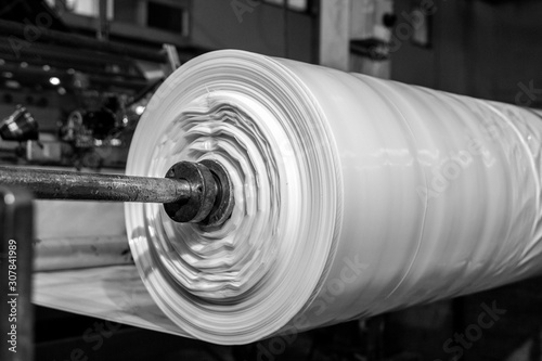 B&W imagery of spool of plastic packaging sheet heavy duty for industrial use outdoors. wrapped around a metal pole ready to feed into a machine for cutting into shape or printing logos or branding