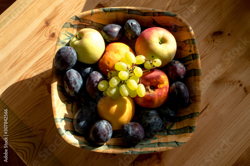 Flat still life plum apples grapes in a wooden stand on a wooden table lit by morning light